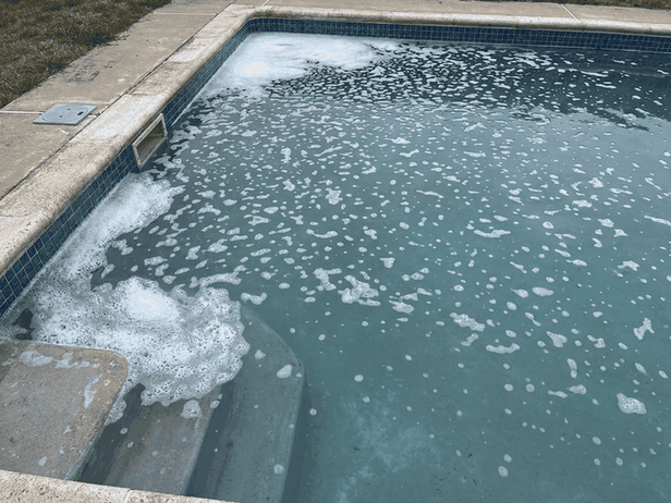 White foam floating on pool water along the tile line